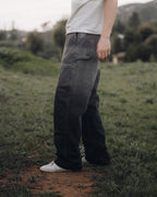 Person wearing dark pants and a light shirt standing on a dirt path in a natural setting.